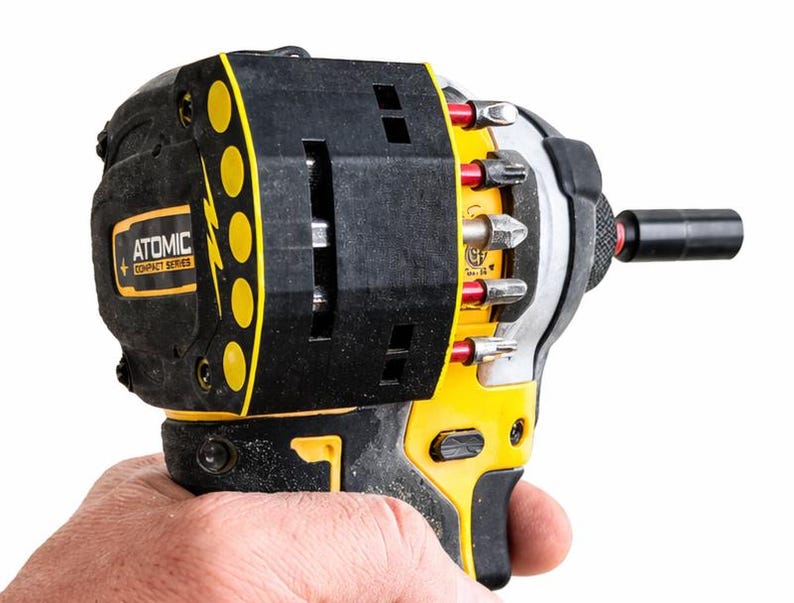 May include: A black and yellow Atomic Compact Series impact driver with various bits attached. The tool has a black handle and a yellow accent. The text "ATOMIC COMPACT SERIES" is visible on the side of the tool.