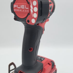 May include: A red and black cordless impact driver with the text "FUEL BRUSHLESS" on the head. The battery pack reads "LITHIUM-ION 18V 6.0 Ah".