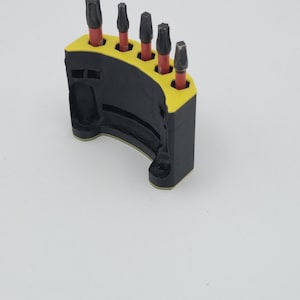 May include: A black and yellow bit holder with five dark metal bits. The holder is curved and has a yellow interior. The bits are arranged in a row, each with a red base.