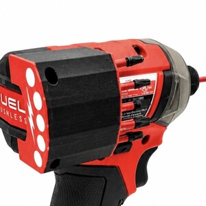 Puede incluir: Un atornillador de impacto sin escobillas FUEL rojo y negro. La herramienta tiene un mango negro y un cuerpo rojo con la palabra "FUEL" y un logotipo de rayo. La herramienta tiene una cubierta de pl&aacute;stico transparente y una broca negra.