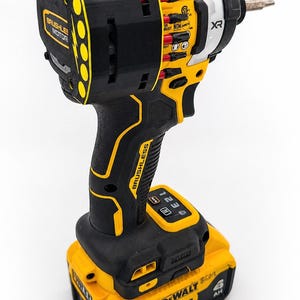May include: A black and yellow cordless impact driver with a drill bit attached. The tool has the text "BRUSHLESS MOTOR" and "DEWALT" printed on it. The battery is labeled "20V".