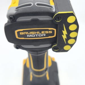 May include: A yellow, gray, and black cordless drill with the words "Brushless Motor" in a gold rectangle. The drill has a black side piece with yellow circles and a lightning bolt design.