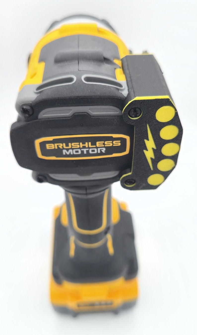 May include: A yellow, gray, and black cordless drill with the words "Brushless Motor" in a gold rectangle. The drill has a black side piece with yellow circles and a lightning bolt design.