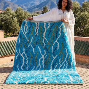 Peut inclure: Un tapis bleu vif avec un motif abstrait blanc et doré. Le tapis est présenté à l'extérieur, mettant en valeur sa texture moelleuse et son design. La palette de couleurs du tapis comprend des nuances de bleu, de blanc et d'or.