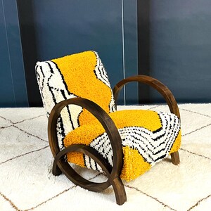 May include: A yellow, black, and white patterned armchair with dark wood curved arms and legs. The chair is sitting on a white rug with a diamond pattern.