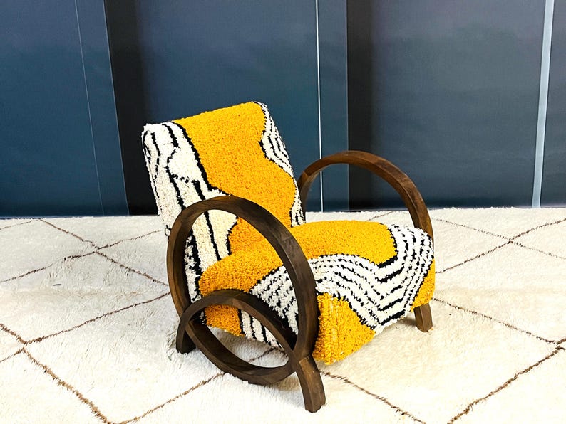 May include: A yellow, black, and white patterned armchair with dark wood curved arms and legs. The chair is sitting on a white rug with a diamond pattern.