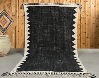 May include: Black and white rug with a geometric pattern. The rug has a fringe border and is made of a soft, textured material.