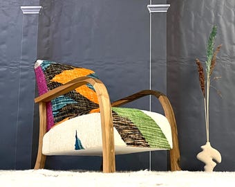 May include: A wooden armchair with a colorful patterned fabric upholstery. The chair has a curved back and arms, and is set against a gray wall.