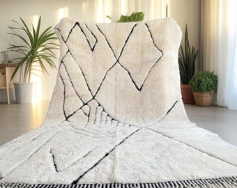 Könnte beinhalten: Ein cremefarbener Teppich mit geometrischem Muster aus schwarzen Linien und Fransen. Der Teppich hat ein Diamanten- und eckiges Design. Die Fransen sind schwarz und weiß. Der Teppich besteht aus einem weichen, strukturierten Material.