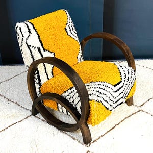 May include: A yellow, black, and white patterned armchair with dark wood curved arms and legs. The chair is sitting on a white rug with a diamond pattern.