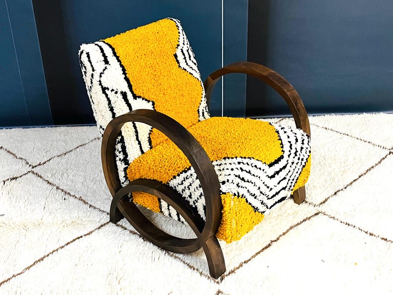 May include: A yellow, black, and white patterned armchair with dark wood curved arms and legs. The chair is sitting on a white rug with a diamond pattern.
