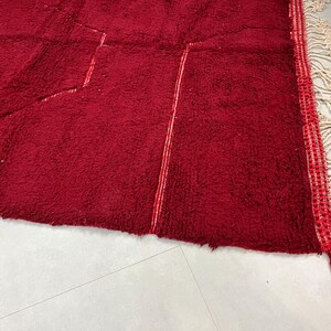 Puede incluir: Una alfombra roja con un patr&oacute;n geom&eacute;trico y flecos blancos. La alfombra tiene una textura suave y mullida.