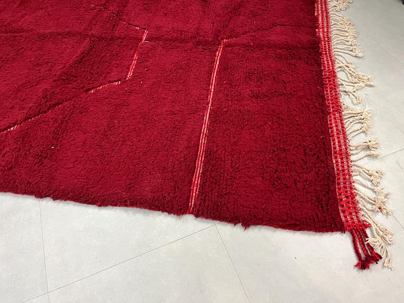 Puede incluir: Una alfombra roja con un patr&oacute;n geom&eacute;trico y flecos blancos. La alfombra tiene una textura suave y mullida.