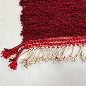 Puede incluir: Una alfombra roja con flecos blancos y rojos. La alfombra tiene una superficie texturizada y esponjosa.