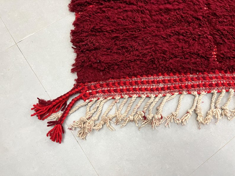 Puede incluir: Una alfombra roja con flecos blancos y rojos. La alfombra tiene una superficie texturizada y esponjosa.