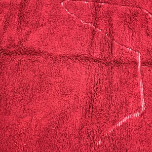 Puede incluir: Primer plano de una alfombra de ba&ntilde;o roja y peluda con un contorno blanco de una forma.