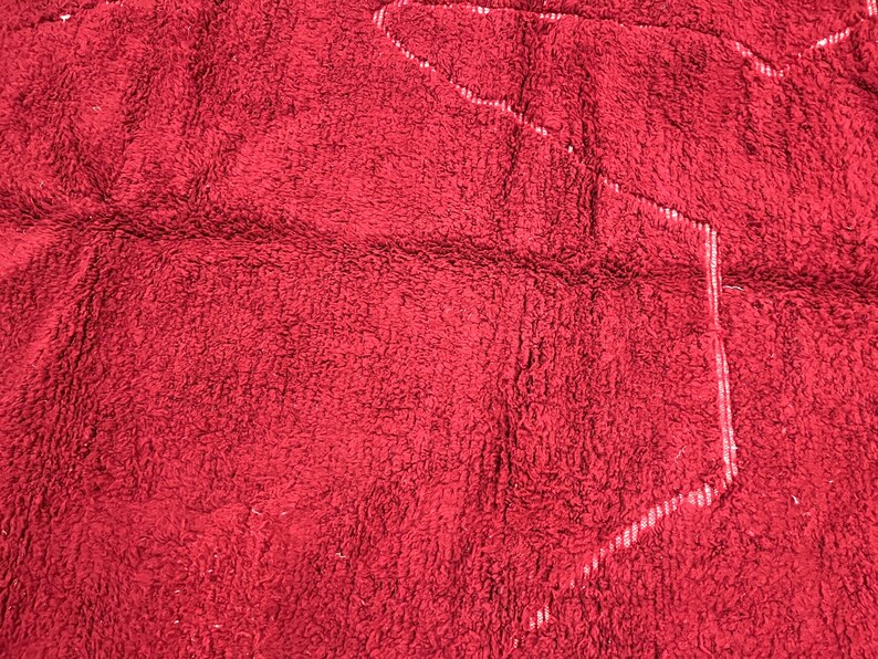 Puede incluir: Primer plano de una alfombra de ba&ntilde;o roja y peluda con un contorno blanco de una forma.