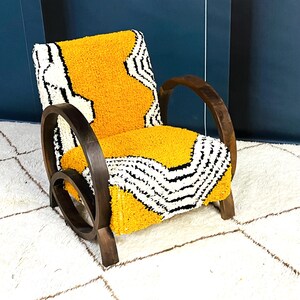 May include: A yellow and black patterned armchair with dark wood curved arms and legs. The chair is sitting on a white rug with a geometric pattern.