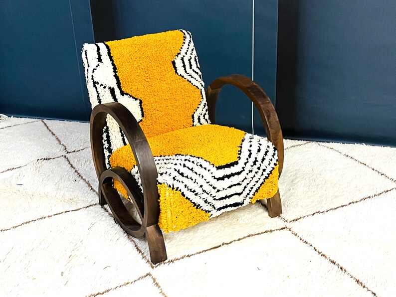 May include: A yellow and black patterned armchair with dark wood curved arms and legs. The chair is sitting on a white rug with a geometric pattern.