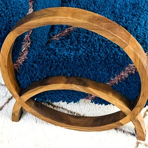 May include: A wooden towel rack with two circular rings. The rack is made of natural wood and has a rustic look. A blue and red striped towel is draped over the rack.