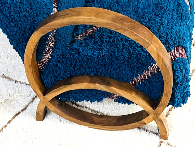 May include: A wooden towel rack with two circular rings. The rack is made of natural wood and has a rustic look. A blue and red striped towel is draped over the rack.