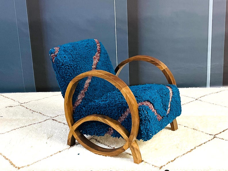 May include: A teal blue armchair with a curved wooden frame and a plush, textured fabric. The chair is sitting on a white rug with a diamond pattern.
