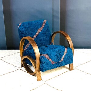 May include: A teal blue armchair with a brown wooden frame and curved arms. The chair is upholstered in a fuzzy fabric with a pink and brown pattern.