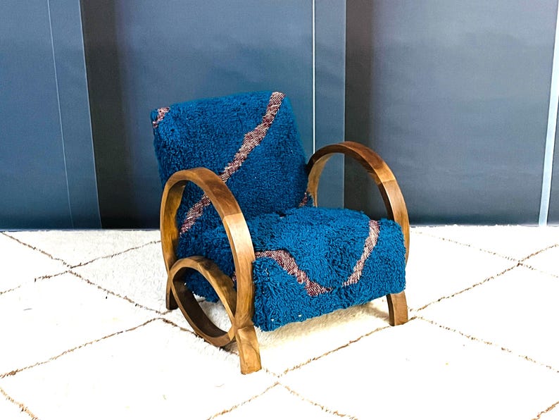 May include: A teal blue armchair with a brown wooden frame and curved arms. The chair is upholstered in a fuzzy fabric with a pink and brown pattern.