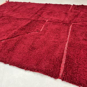 Puede incluir: Una alfombra de pelo rojo oscuro con un patr&oacute;n &uacute;nico de costuras que crean formas geom&eacute;tricas. La alfombra tiene una textura suave y mullida.
