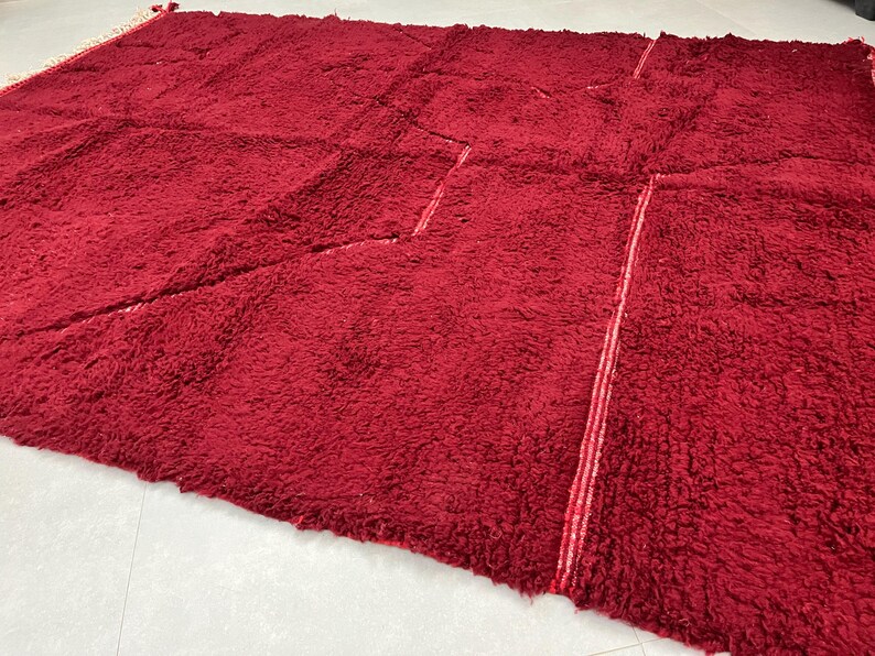 Puede incluir: Una alfombra de pelo rojo oscuro con un patr&oacute;n &uacute;nico de costuras que crean formas geom&eacute;tricas. La alfombra tiene una textura suave y mullida.