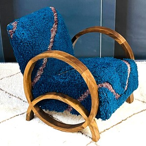 May include: A teal blue armchair with a wooden frame. The chair has a unique curved design with a rounded back and arms. The chair is upholstered in a soft, fuzzy fabric.