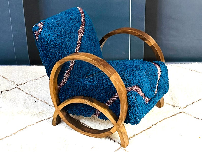 May include: A teal blue armchair with a wooden frame. The chair has a unique curved design with a rounded back and arms. The chair is upholstered in a soft, fuzzy fabric.