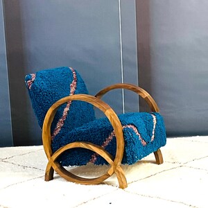 May include: A teal blue armchair with a curved wooden frame and a plush, textured fabric. The chair is sitting on a white rug.