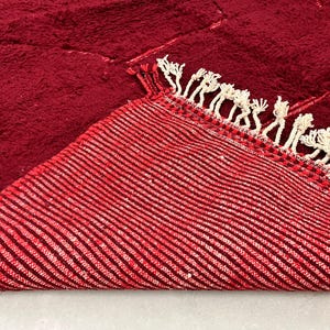 Puede incluir: Primer plano de una alfombra de rayas rojas y blancas con borde de flecos. La alfombra est&aacute; doblada por la mitad, mostrando la parte inferior de la alfombra.