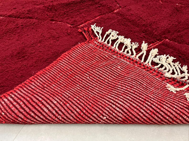 Puede incluir: Primer plano de una alfombra de rayas rojas y blancas con borde de flecos. La alfombra est&aacute; doblada por la mitad, mostrando la parte inferior de la alfombra.