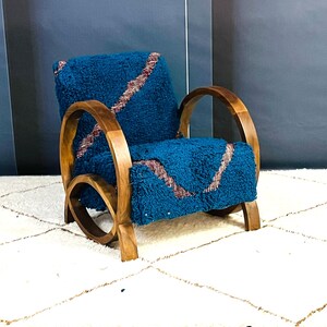 May include: A teal blue armchair with a curved wooden frame and a plush, textured fabric. The fabric has a pattern of pink and white lines.