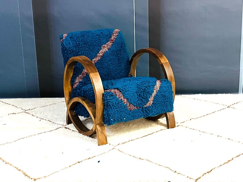 May include: A teal blue armchair with a curved wooden frame and a plush, textured fabric. The fabric has a pattern of pink and white lines.