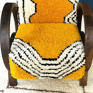 May include: A yellow and white patterned chair with dark brown wooden arms and legs. The chair is upholstered in a thick, fuzzy fabric.