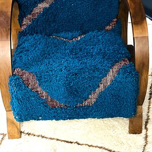 May include: A teal blue and burgundy patterned cushion sits on a wooden chair with curved arms. The chair is on a white and brown rug.