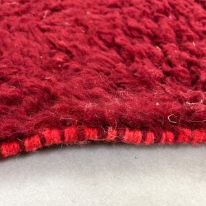 Puede incluir: Primer plano de una alfombra de color rojo intenso con un borde tejido rojo y blanco. La alfombra tiene una textura suave y peluda.