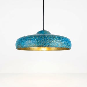 Peut inclure: Suspension luminaire avec une finition bleue martelée et un intérieur doré. Le luminaire a une forme de bol large et peu profond et est suspendu à un cordon noir. Le design est moderne et décoratif, idéal pour l'éclairage intérieur.