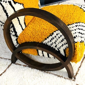 May include: A wooden armchair with a yellow and black patterned cushion. The chair has a unique curved design and is upholstered in a soft, plush fabric.
