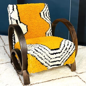 May include: A yellow and white patterned armchair with dark wood arms and a curved wooden base. The chair is sitting on a white rug.