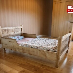 May include: A rustic, wooden toddler bed with a headboard and footboard. The bed frame is made of light-colored wood. The bed is made up with a floral patterned blanket and a blue pillow. The bed is approximately 60 inches long.