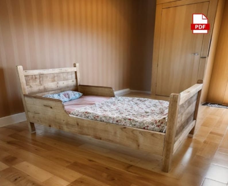 May include: A rustic, wooden toddler bed with a headboard and footboard. The bed frame is made of light-colored wood. The bed is made up with a floral patterned blanket and a blue pillow. The bed is approximately 60 inches long.