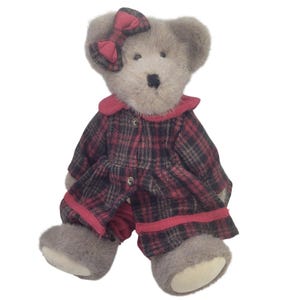 May include: A plush teddy bear with a gray body and a red plaid outfit. The bear wears a red bow and a matching collar and trim on the outfit. The outfit has black buttons and the bear has a black nose.