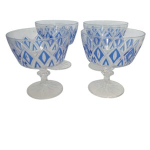 May include: Four clear glass dessert bowls with blue diamond patterns. The bowls have a stemmed base and a wide, shallow bowl shape. The blue pattern is a repeating geometric design. The bowls are arranged on a white background.