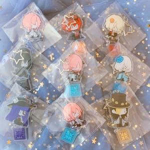 May include: A collection of ten colorful anime character keychains with star-shaped charms. The keychains are packaged in clear plastic bags and displayed on a blue background with white stars.
