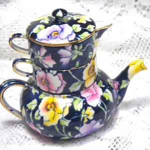 Puede incluir: Una tetera de porcelana azul y blanca con un diseño floral. La tetera tiene una tapa y un asa. La tetera está apilada sobre dos tazas con asas.
