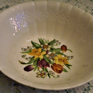 May include: A white ceramic bowl with a floral design featuring yellow daffodils, purple tulips, and white lily of the valley.